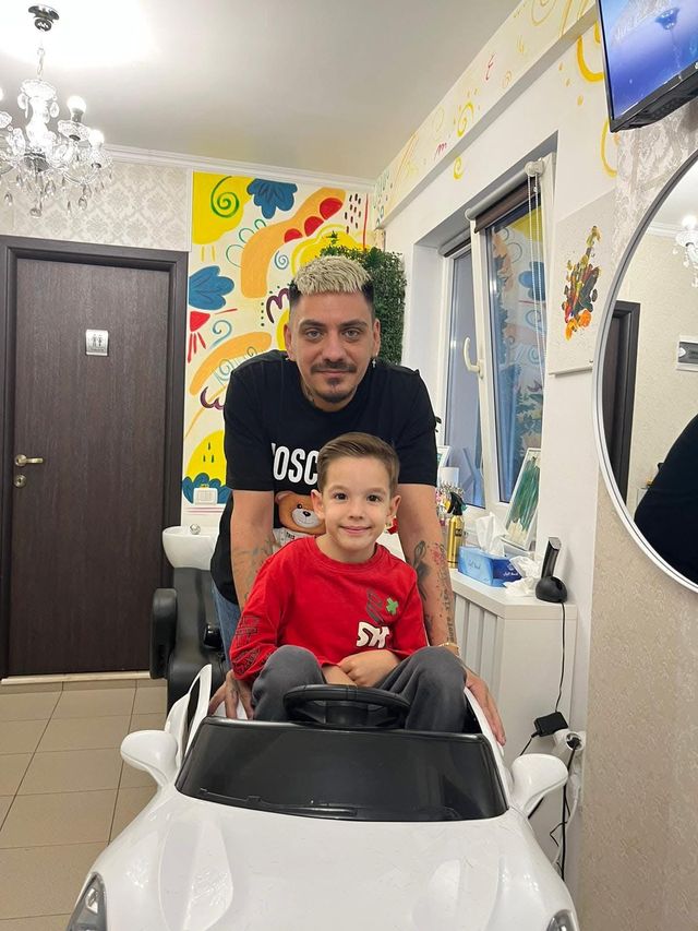 Frizerul și un băiețel zâmbitor, așezat pe scaunul în formă de mașinuță albă