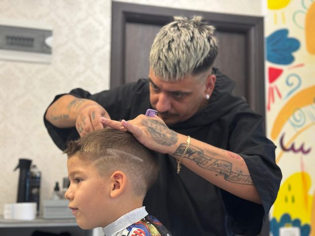 Frizerul lucrează cu atenție la tunsoarea unui băiat